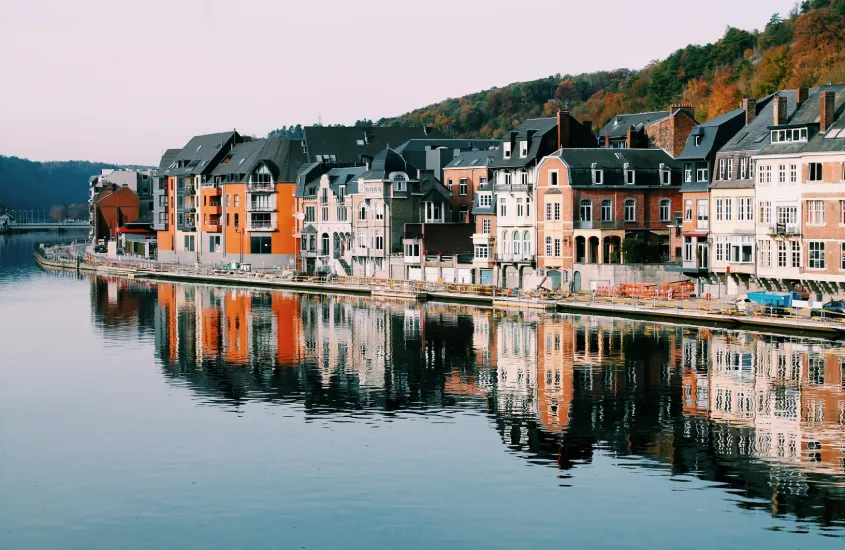 Reflexo de prédios coloridos na água de um canal, em uma cidade europeia. As casas têm tons de tijolo e laranja