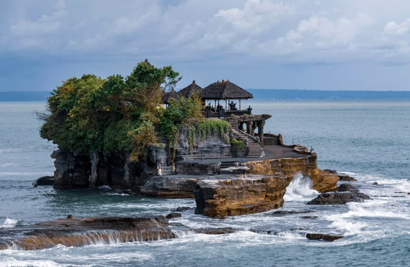 Um templo balinês localizado em uma rocha à beira-mar, cercado por ondas e vegetação