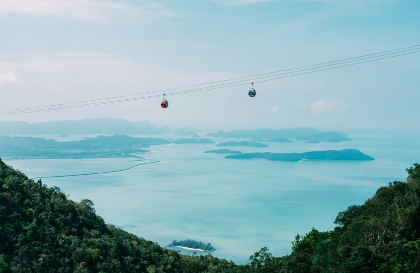 Teleféricos sobre um mar azul claro, com ilhas ao fundo, criando um panorama deslumbrante para quem busca aventuras românticas