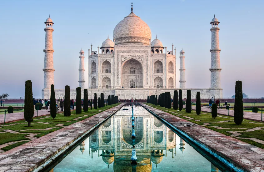 O Taj Mahal refletindo em uma fonte, cercado por jardins bem cuidados, simbolizando o amor eterno