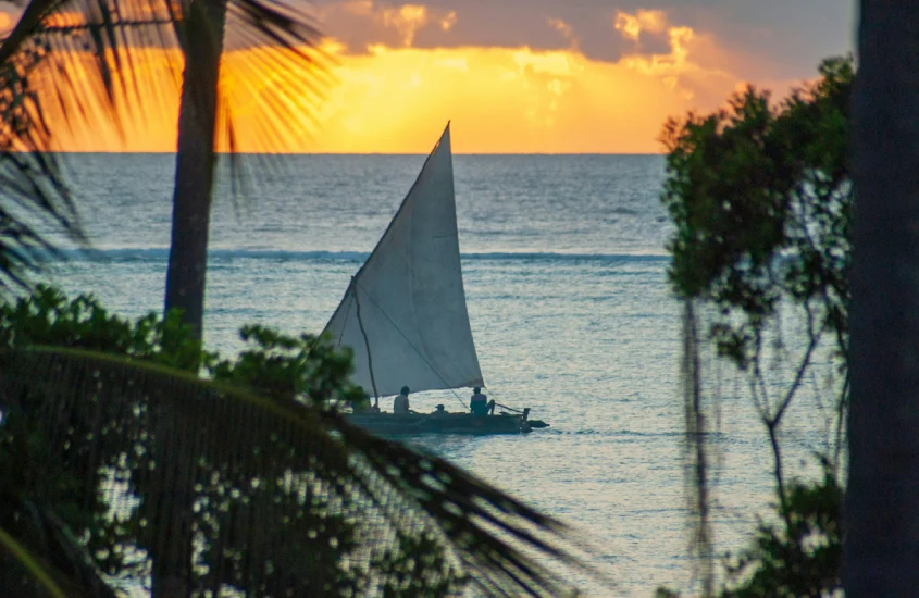 Barco a vela navegando em águas calmas ao pôr do sol, simbolizando a tranquilidade e a beleza de uma viagem romântica a dois em um destino exótico