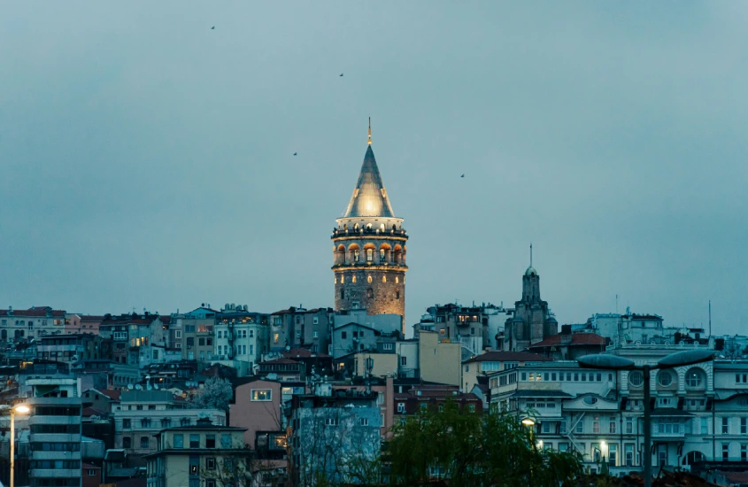 Torre de Gálata iluminada, com prédios ao redor, contrastando com o céu nublado, em uma das vistas mais conhecidas de Istambul