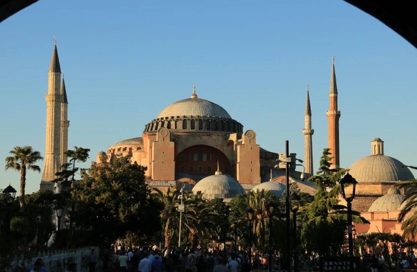 A imponente Hagia Sophia em Istambul, com sua arquitetura bizantina, cercada por minaretes, em um dia ensolarado com muitas pessoas visitando o local histórico