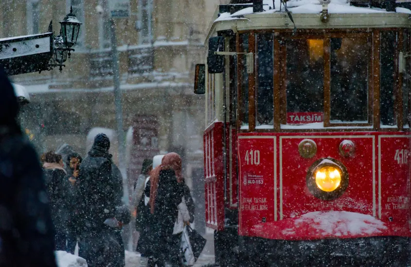 Bonde vermelho de Taksim circulando em uma rua de Istambul durante uma nevasca, com pedestres ao redor