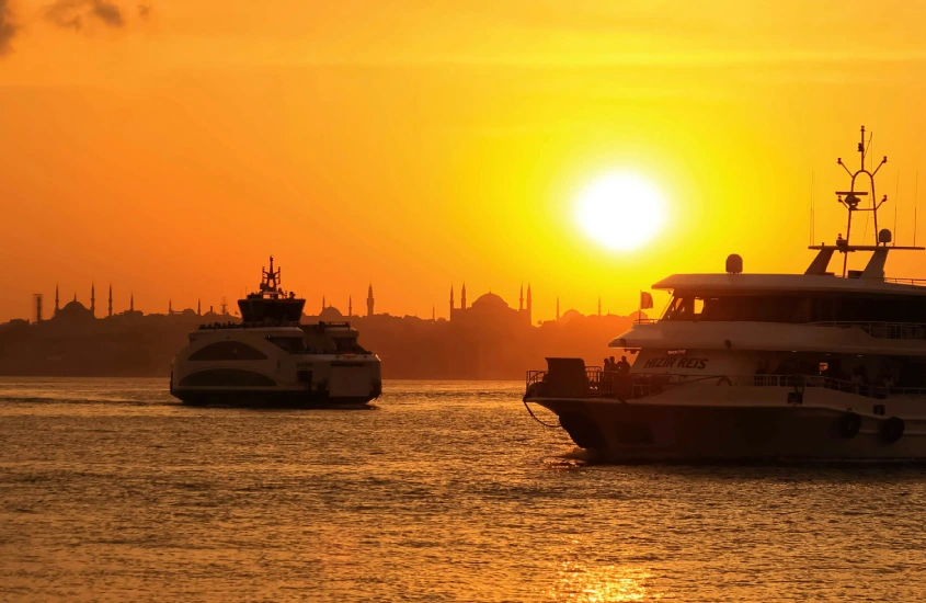 Barcos navegando pelo Estreito de Bósforo ao pôr do sol, com as silhuetas das mesquitas ao fundo em Istambul