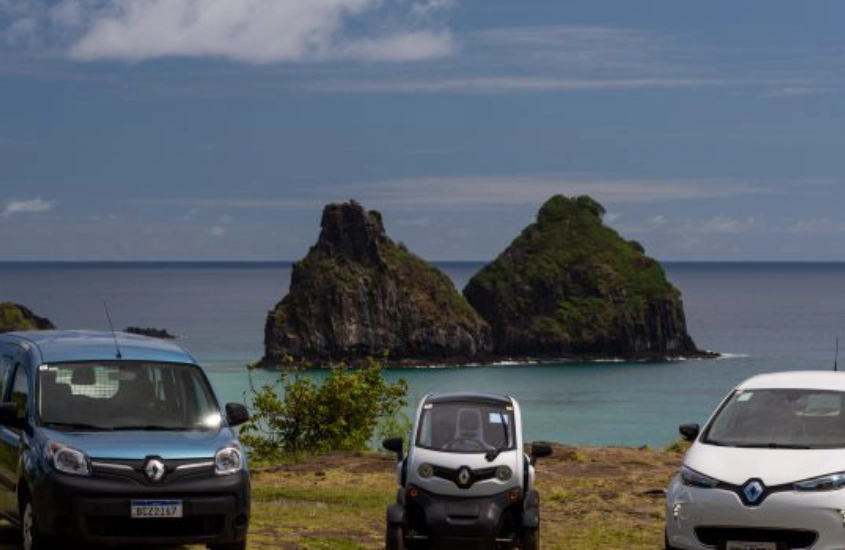 Três carros elétricos estacionados com vista para as ilhas Dois Irmãos, simbolizando sustentabilidade e mobilidade em Fernando de Noronha.