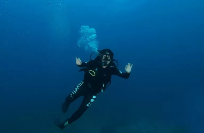 Mergulhador de preto posando submerso, com bolhas subindo ao seu redor em águas profundas de Noronha.