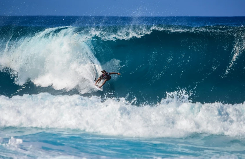 Surfista em ação, pegando uma onda gigante azul com maestria e equilíbrio, em meio à força do mar.