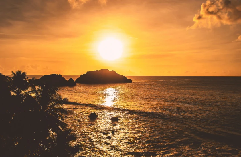 Pôr do sol em Noronha, com o céu em tons alaranjados e o sol refletindo sobre o mar, criando uma atmosfera calma e intensa.