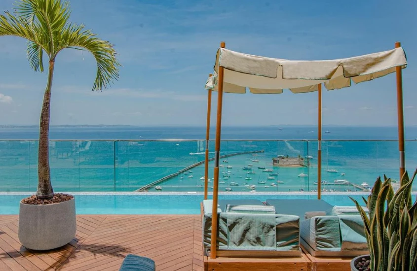 Piscina de borda infinita com vista para o mar em Salvador, cercada por uma estrutura de madeira e uma palmeira ao lado.