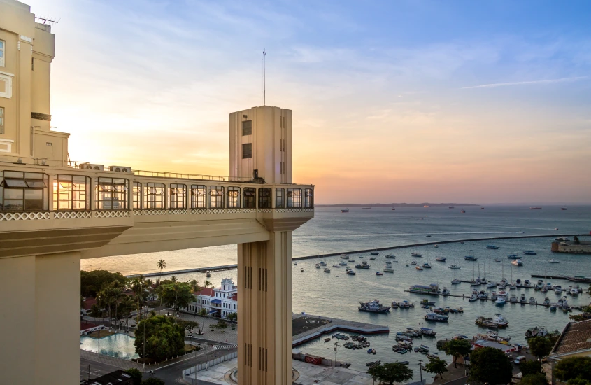 Elevador Lacerda ao pôr do sol, com vista para a Baía de Todos os Santos e barcos ancorados no mar tranquilo.