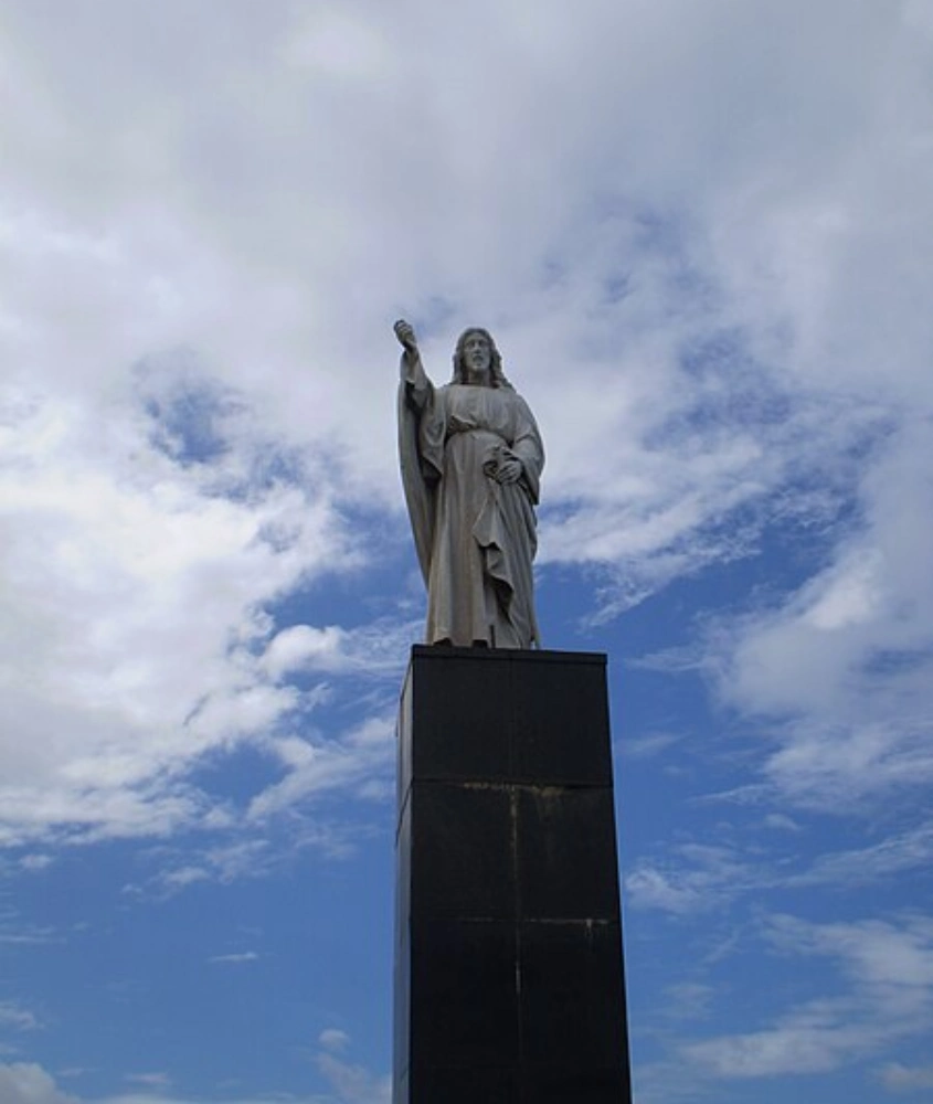 Estátua de Jesus Cristo em Salvador, destacando-se contra um céu nublado com tons de azul e branco.