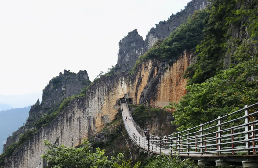 Ponte suspensa de Zhangjiajie, rodeada por penhascos íngremes e vegetação densa em uma paisagem montanhosa.