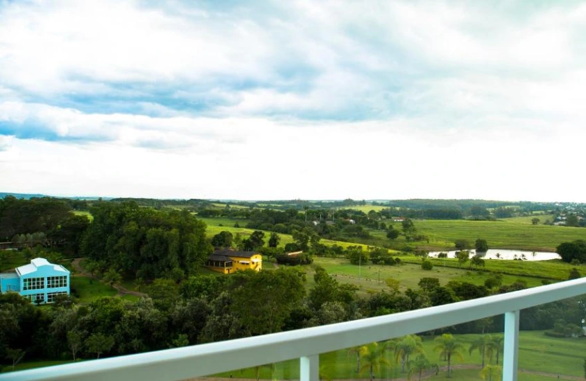 Varanda com vista para um campo verdejante e várias construções coloridas ao longe, em meio a uma paisagem natural.