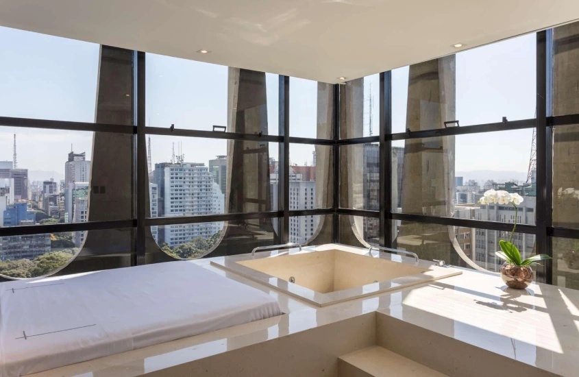 Banheira de hidromassagem em uma área envidraçada com vista panorâmica para os prédios de São Paulo, com decoração minimalista e luz natural.