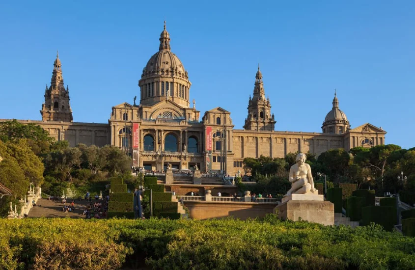 Em um dia ensolarado, fachada de museu com estátuas, plantas e árvores ao redor