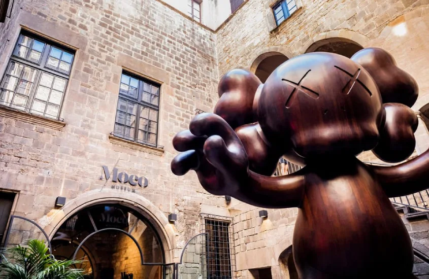 Em um dia de sol, parte exterior de museu em Barcelona com obra de cobre e plantas ao redor