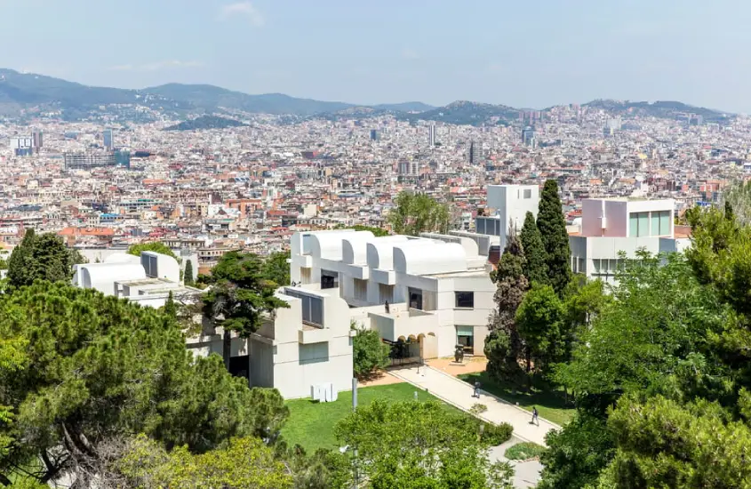 Em um dia ensolarado, fachada do museu em Barcelona com árvores, plantas e cidade atrás