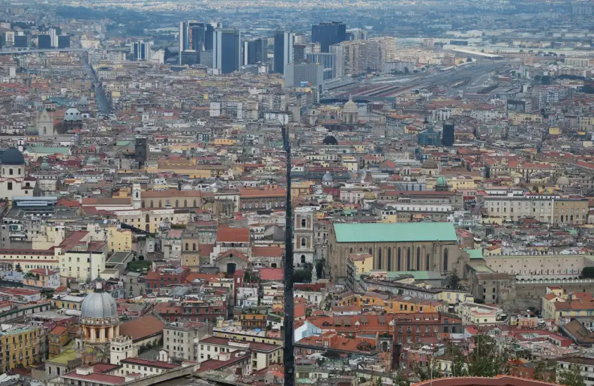 Vista panorâmica de Nápoles com seus prédios antigos, cúpulas de igrejas e a modernidade dos edifícios mais altos ao fundo.