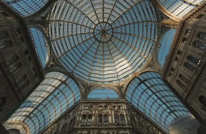 Teto de vidro e metal na Galleria Umberto I, com arquitetura imponente e simetria que destaca a luz natural entrando no espaço.