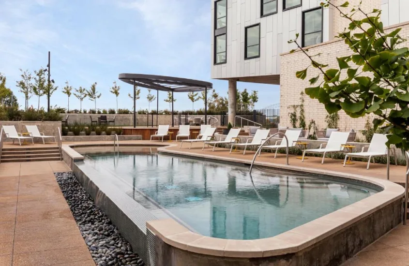 Piscina moderna ao ar livre de um hotel em Memphis, rodeada por cadeiras de descanso e uma área arborizada ao fundo.