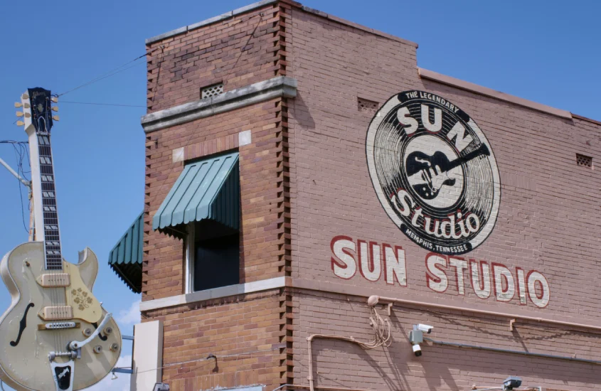 Fachada do Sun Studio em Memphis, Tennessee, com tijolos vermelhos, toldos verdes e o icônico logotipo pintado na parede, acompanhado de uma guitarra gigante suspensa.