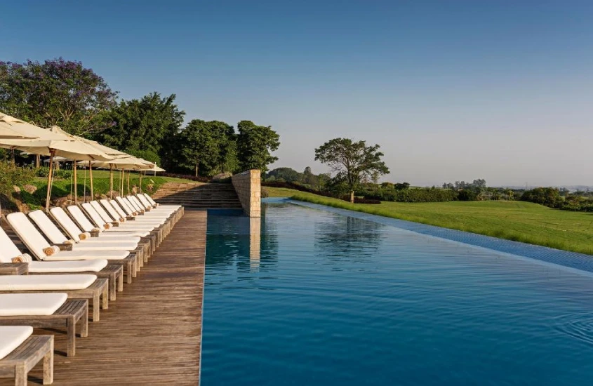 Durante um dia de sol, área de piscina com espreguiçadeiras, guarda-sóis e árvores ao redor