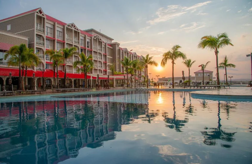 Durante o pôr do sol, área de lazer de hotel com piscina, espreguiçadeiras e árvores ao redor