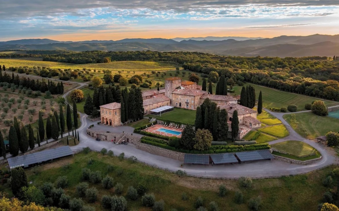 Vista aérea de um dos hotéis vinícolas na Toscana, cercada por ciprestes, vinhedos e paisagens montanhosas, iluminada pela luz suave do fim de tarde