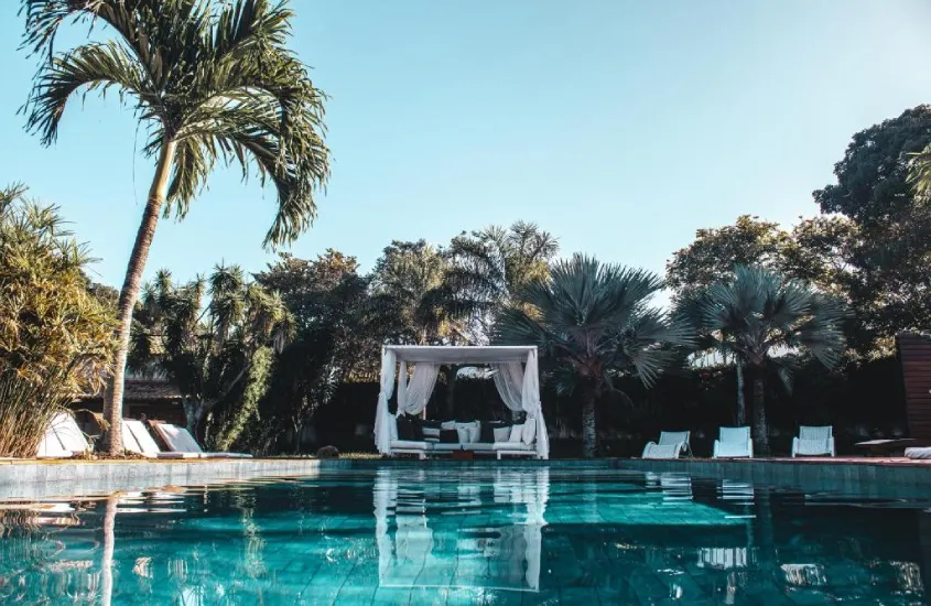 Em um dia ensolarado, área de lazer de hotel com recreação infantil em Búzios com piscina, espreguiçadeiras, tenda coberta e árvores ao redor