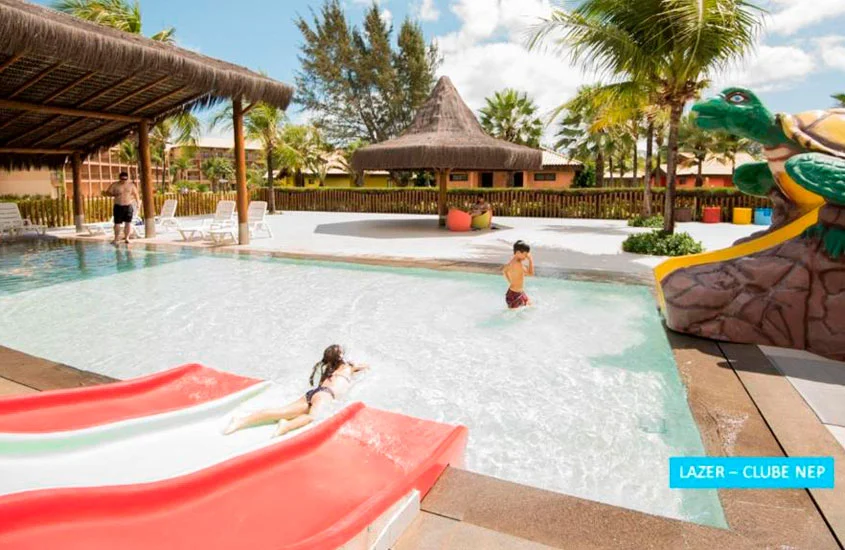 Em um dia de sol, crianças curtindo a piscina com espreguiçadeiras, brinquedos de água e árvores ao redor