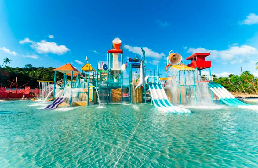 Em um dia de sol, área de piscina de um hotel com recreação infantil no nordeste com escorregadores, brinquedos e árvores ao redor