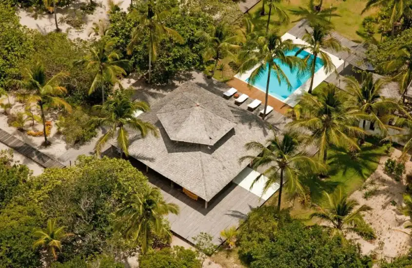 Estrutura central cercada por vegetação tropical e uma ampla piscina com espreguiçadeiras ao fundo, em um cenário de refúgio natural.