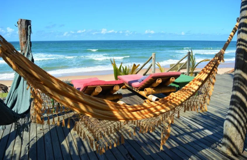 Redes de descanso em um deck de madeira, com vista direta para o mar e cadeiras acolchoadas, em um ambiente de relaxamento à beira da praia.