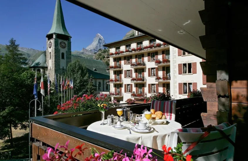 Vista de um terraço com café da manhã montado, destacando o Grand Hotel Zermatterhof e o Matterhorn ao fundo.