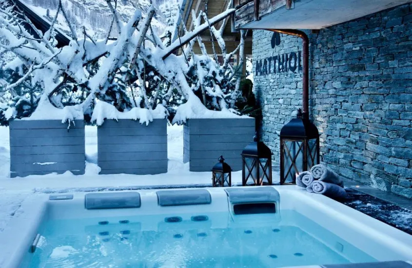 Jacuzzi ao ar livre, rodeada por neve e lanternas decorativas em Matthiol Boutique Hotel, um hotel onde ficar em Zermatt.