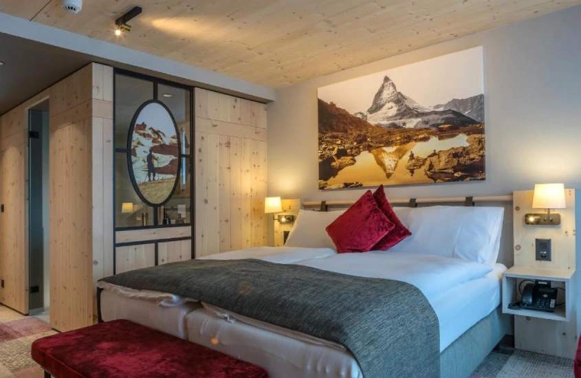 Quarto moderno e aconchegante de um hotel em Zermatt, com detalhes em madeira e uma grande foto do Matterhorn na parede.