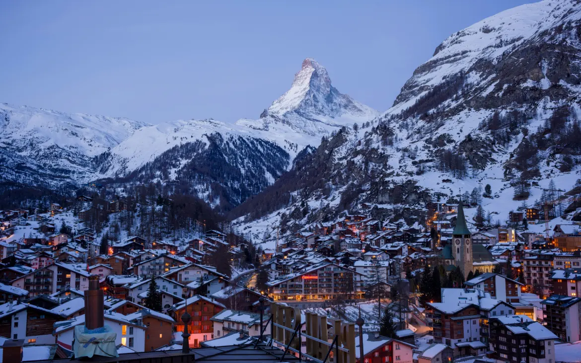 Vista panorâmica de Zermatt à noite, com o icônico Matterhorn ao fundo, sob um céu claro de inverno.