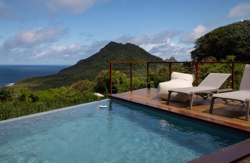 Piscina infinita da Pousada Triângulo Grega, com espreguiçadeiras ao redor e uma vista impressionante das montanhas e do mar.