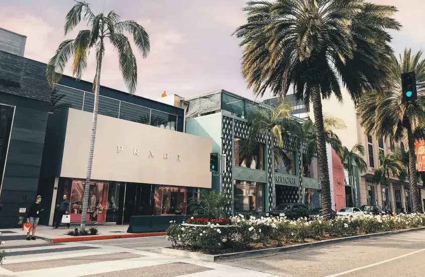 Rua arborizada de Beverly Hills com lojas de grife como Prada e Gucci.