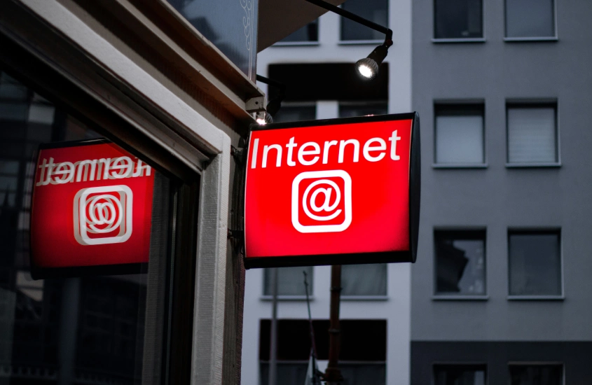 Placa iluminada com a palavra "Internet" em letras brancas sobre fundo vermelho, refletindo na janela de um prédio.