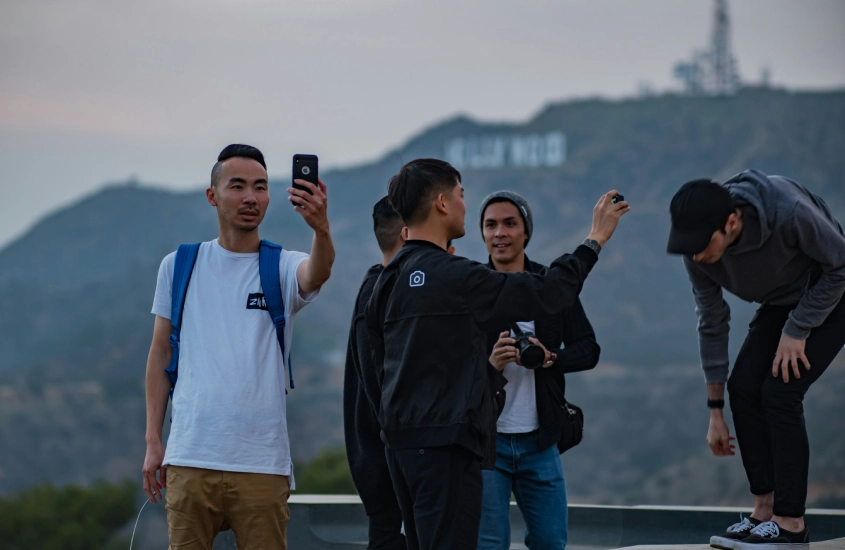 Grupo de jovens tirando selfies em frente à vista de um letreiro famoso em uma colina.