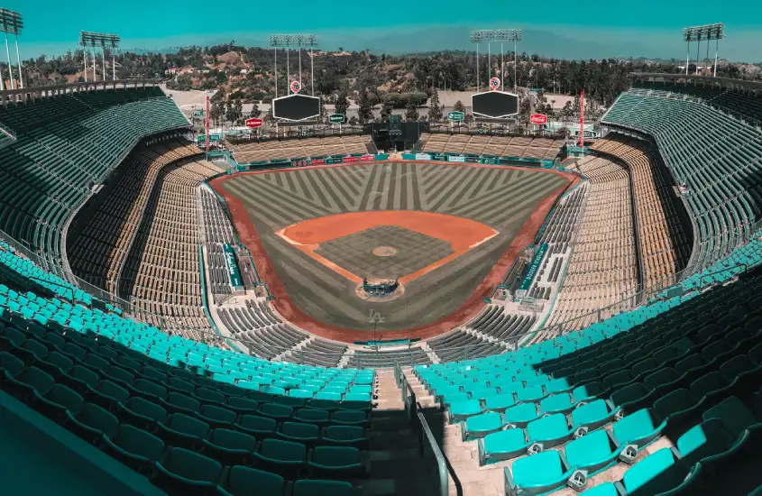 Estádio de beisebol vazio, com assentos turquesa e vista do campo e telões.