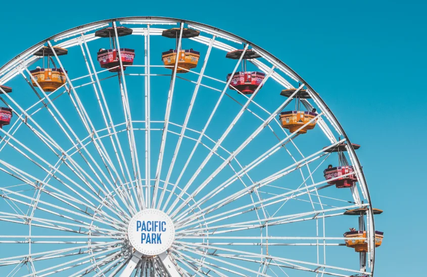 Roda-gigante no Pacific Park, com suas cabines coloridas e céu azul ao fundo, simbolizando diversão à beira-mar.