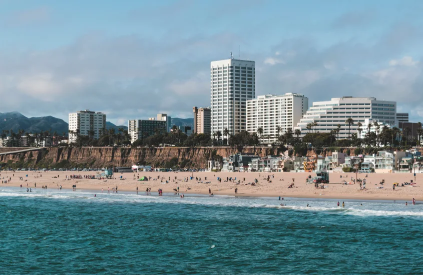 Vista da praia de Santa Mônica com edifícios modernos e falésias ao fundo.