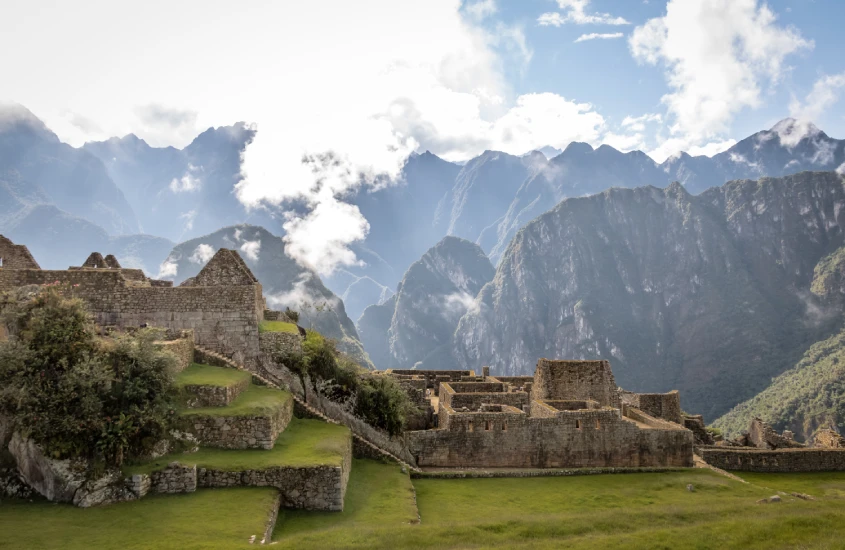 Vista das ruínas de Machu Picchu com a imponente cordilheira dos Andes ao fundo, envolta por nuvens que realçam a grandiosidade do local.