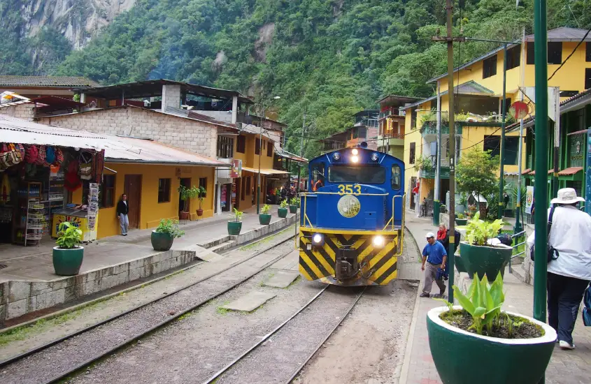 Trem azul e amarelo em Aguas Calientes, estacionado ao lado de construções coloridas, sinalizando o ponto de partida para explorar Machu Picchu.