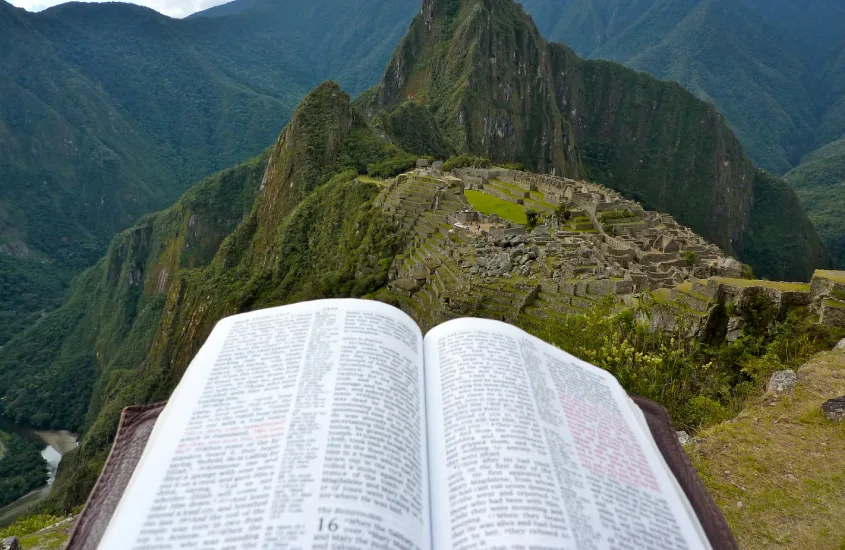 Vista de Machu Picchu com uma bíblia em primeiro plano, destacando as montanhas verdes e os céus azuis ao fundo.