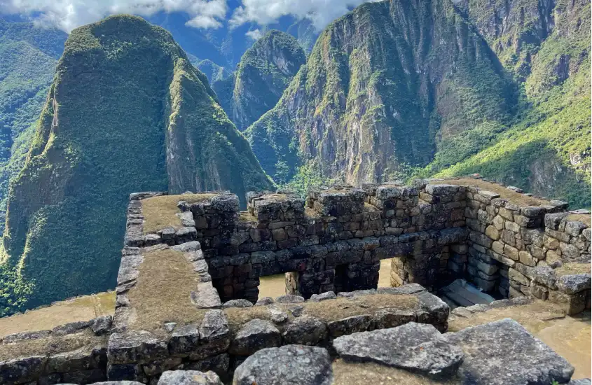 Construções de pedra de Machu Picchu emolduradas por montanhas imponentes sob um céu parcialmente nublado.