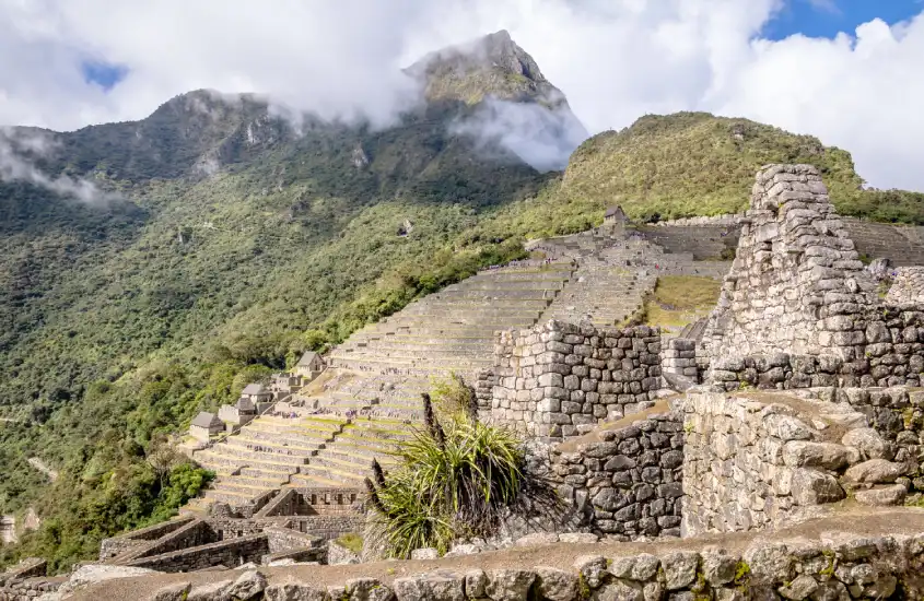 As terraças e construções históricas de Machu Picchu se destacam entre a paisagem montanhosa e o céu claro.